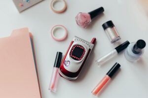 Flat lay of a vintage flip phone with makeup items on a white surface, embodying fashion creativity.