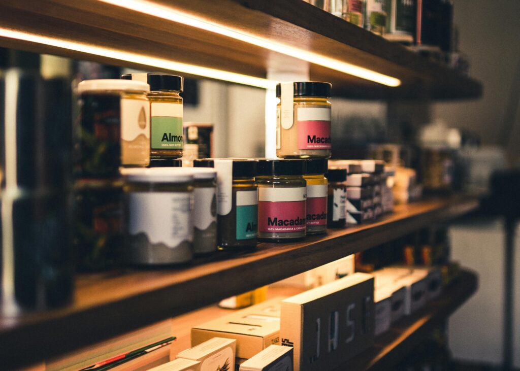 Close-up of artisan almond and macadamia nut butter jars on a wooden shelf in a shop.