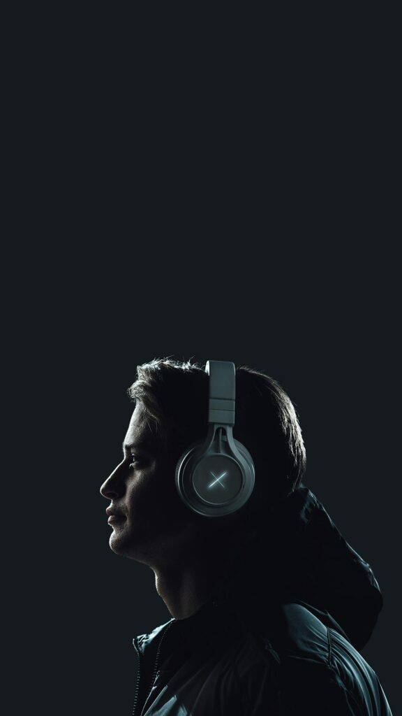 Moody portrait of a young man wearing headphones against a dark studio backdrop.